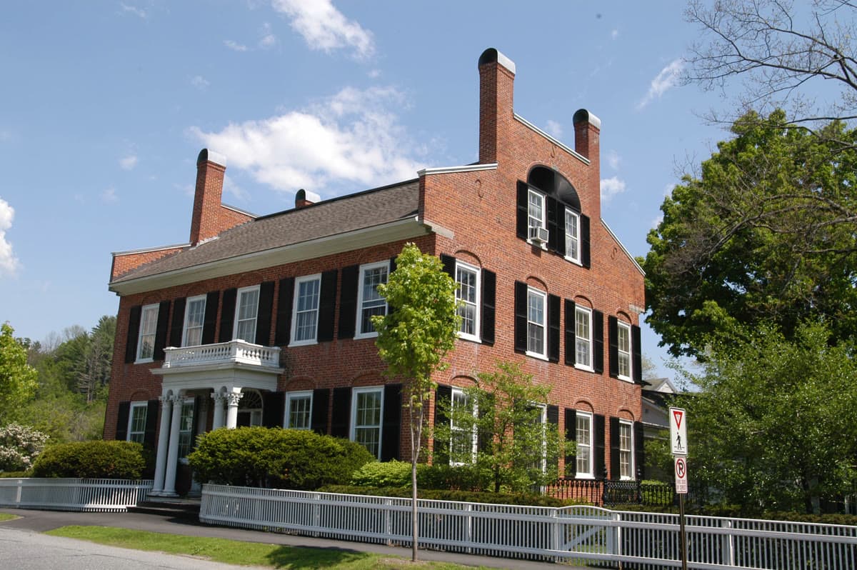 Historic Federal-style brick building in Woodstock Village, Vermont, with columned portico and white picket fence